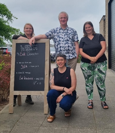 Drie vrouwen en een man staan naast een krijtbord. Hierop staat de tekst: Welkom bij Enik Woerden.