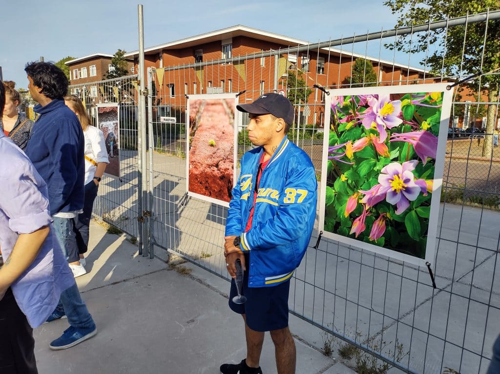 Foto van 2 van de foto's van de tentoonstelling, bevestigd aan een hek. Ervoor staat een persoon.