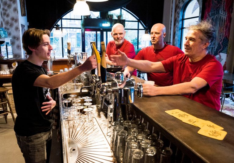 Foto van 3 mensen die aan de bar zitten en 1 persoon die achter de bar staat.