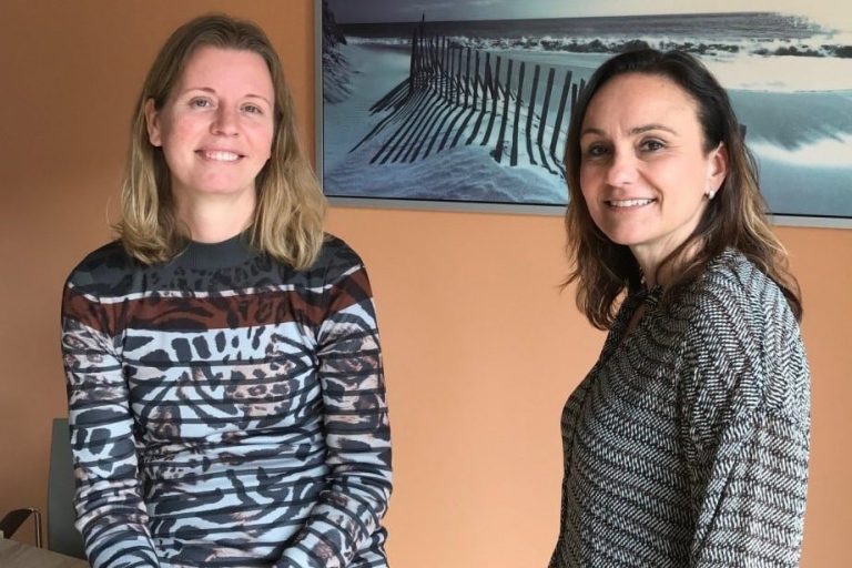 Foto van twee vrouwen die rechtstreeks de camera in kijken.