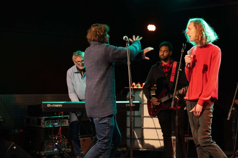 Drie personen op een podium die instructies van een man krijgen