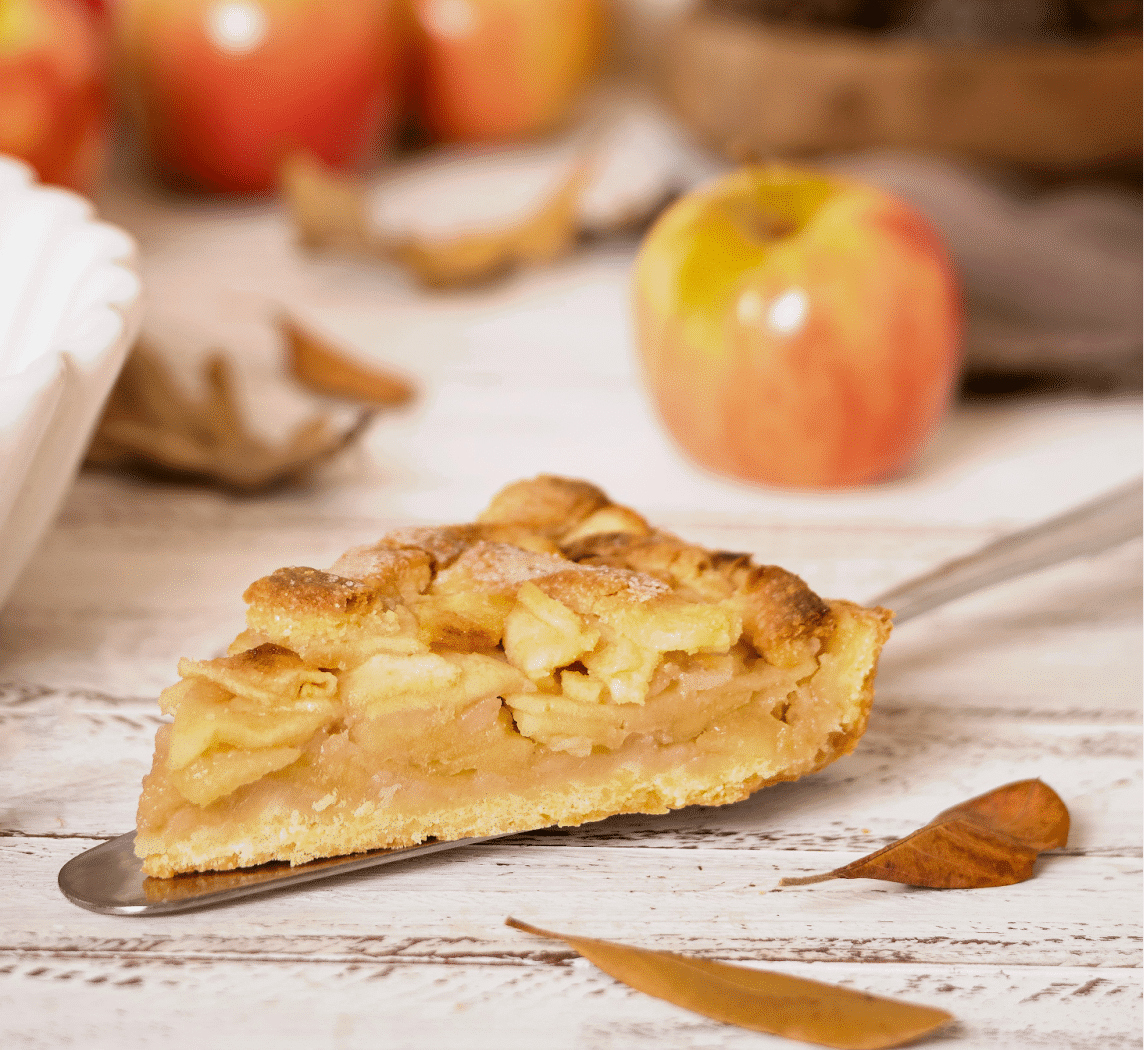 Stukje appeltaart met appels in de achtergrond