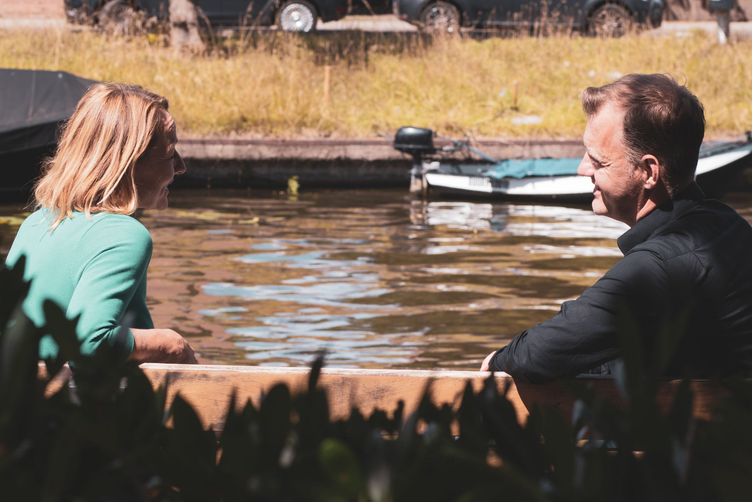 twee personen zitten buiten bij het water en zijn in gesprek