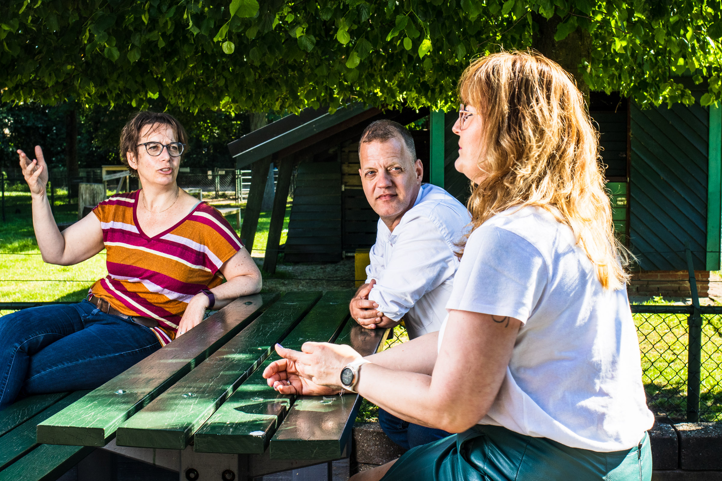 drie mensen zitten buiten aan een tafel