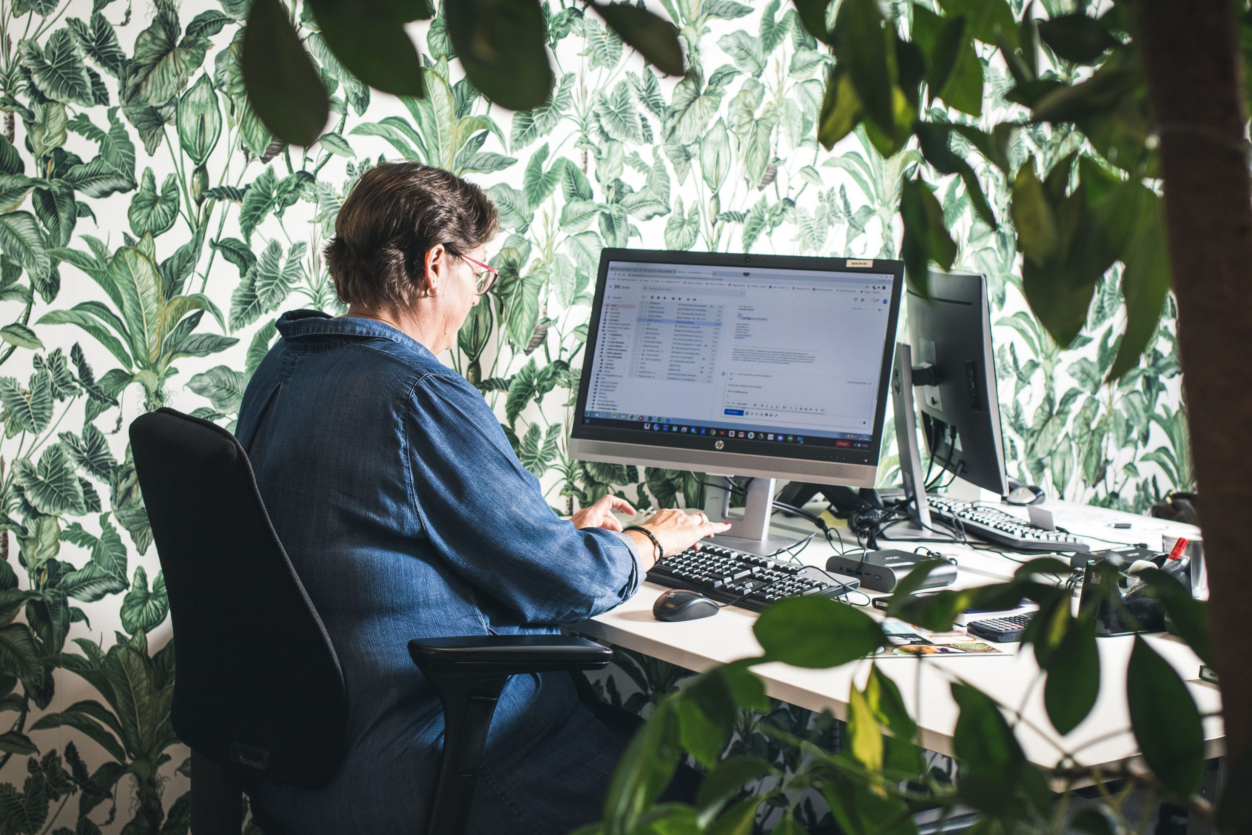 Foto van vrouw aan het werk aan een computer met groene planten op de voorgrond.