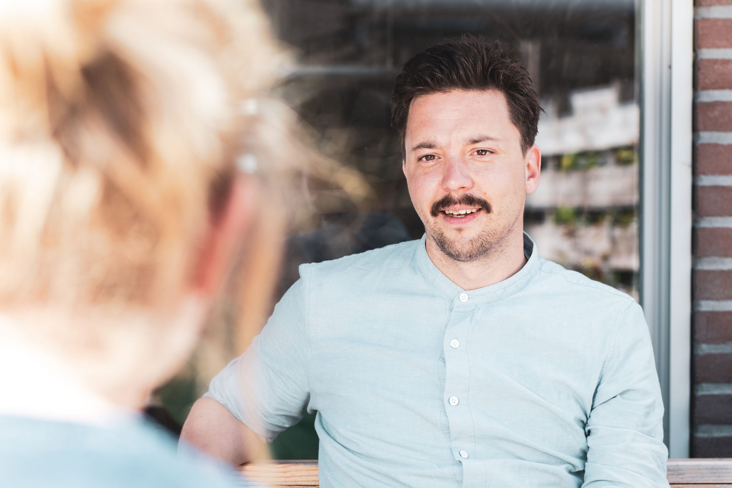 man met een snor en baar is in gesprek met iemand die je van achteren ziet