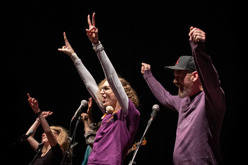Drie mensen hebben hun handen in de lucht terwijl ze aan het zingen zijn.