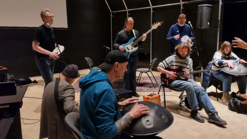 Een groep mensen die met elkaar muziek maakt. Je ziet klankschalen, gitaren en een tamboerijn.