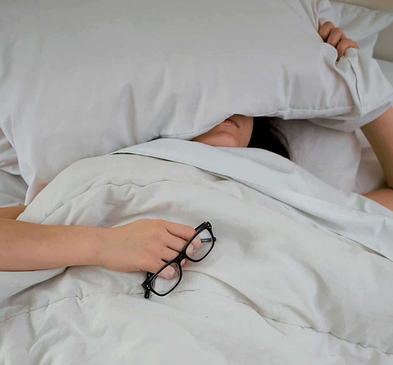 Foto van een persoon in bed met een kussen op het hoofd.